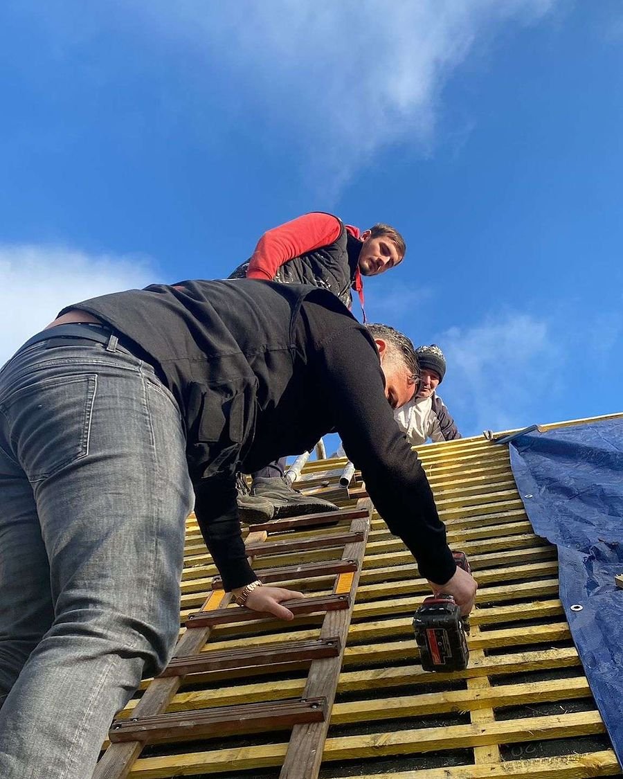 Un compagnon Dujardin visse les liteaux d'une toiture en rénovation, sous le ciel bleu